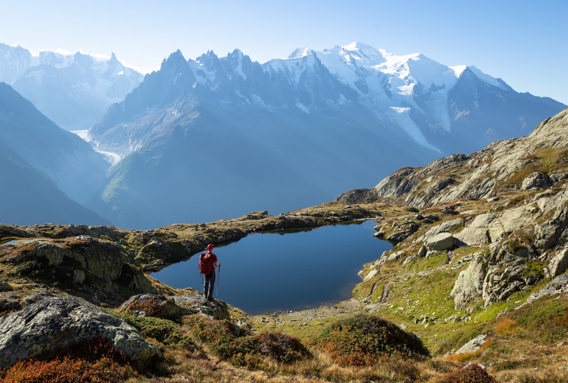 Hiker overlooking Lac Blanc with snow-capped mountains and glacier in the background.