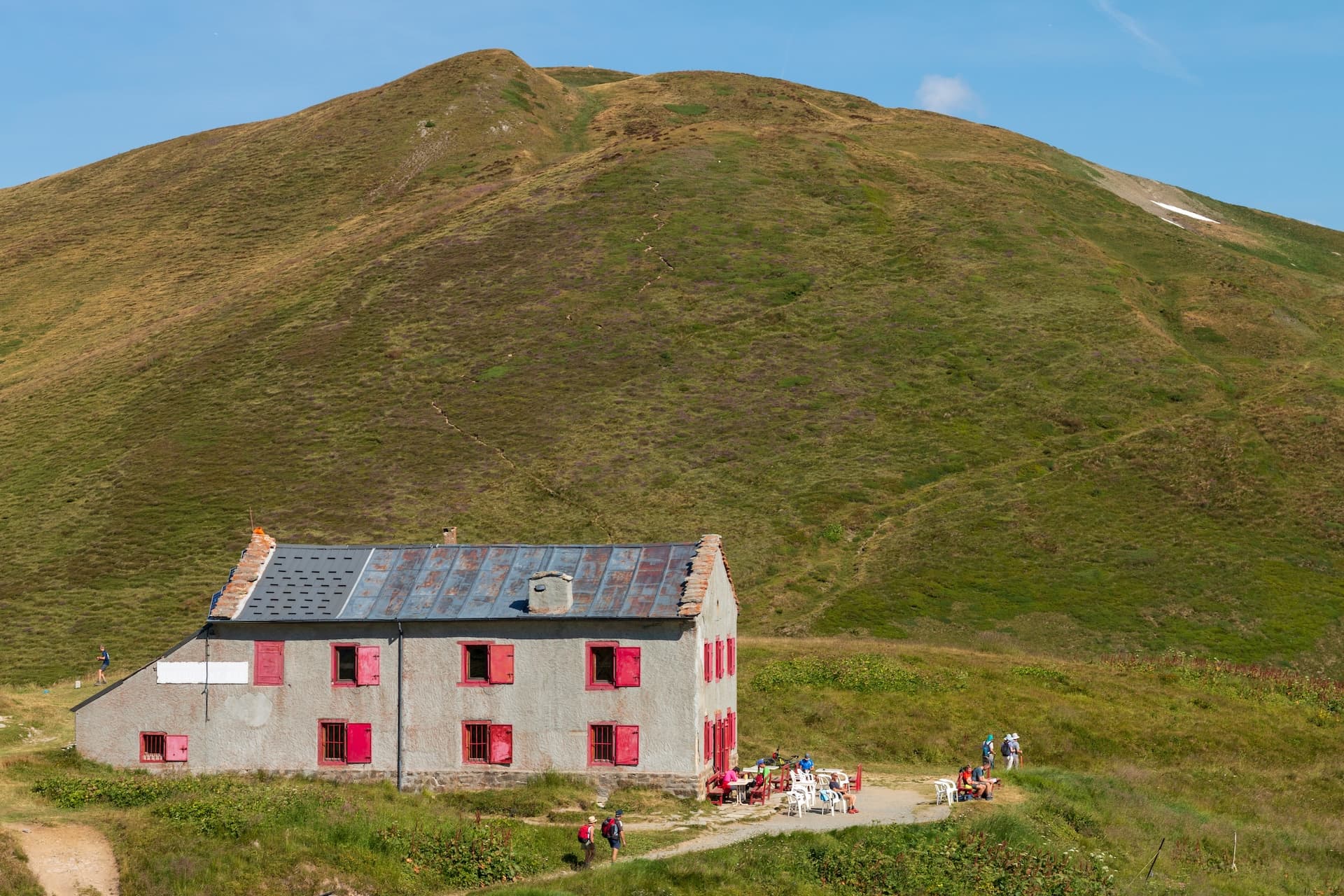 Refuge Col de Balme stone building with red shutters at the base of a grassy mountain.