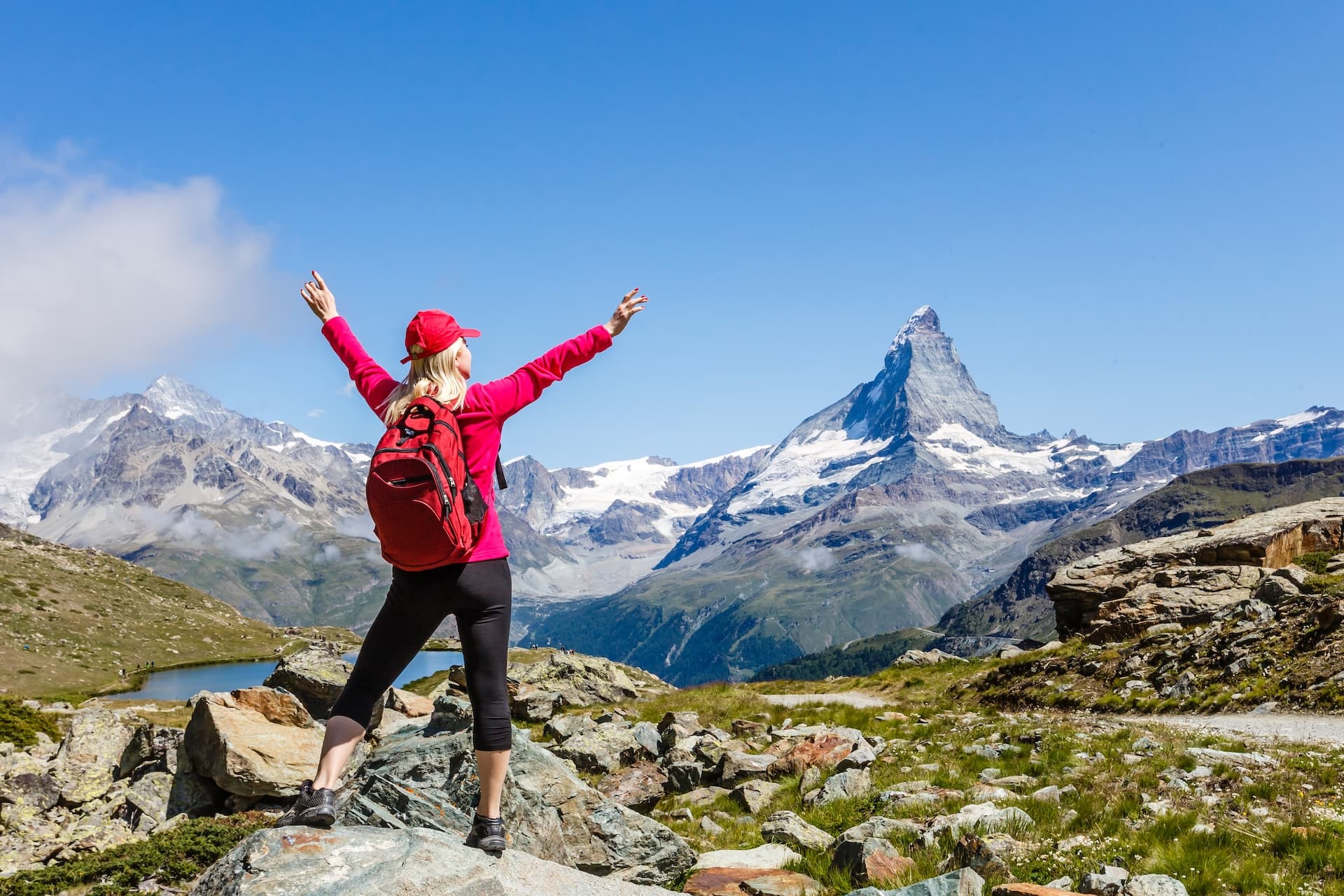 Hiker with arms raised overlooking Riffelsee lake and the Matterhorn mountain in the Alps.