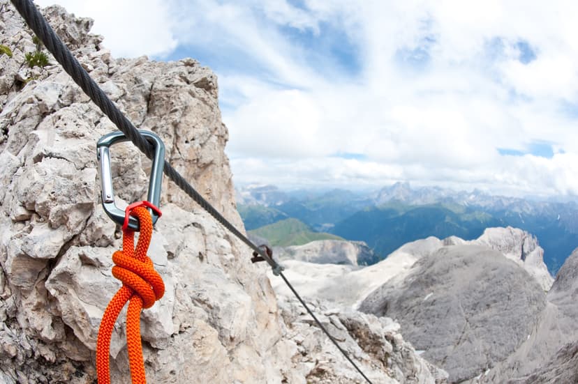 Via ferrata carabiner and orange rope secured to a steel cable on a rocky mountain edge.