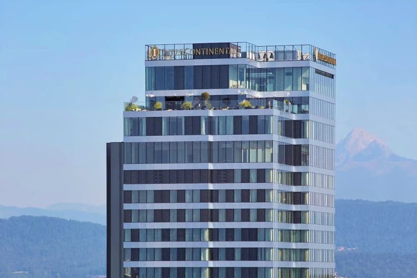 InterContinental Hotel skyscraper exterior with rooftop terrace against a backdrop of hazy mountains.