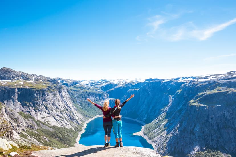 Hikers with arms raised overlooking a deep blue fjord surrounded by steep mountains in Norway.