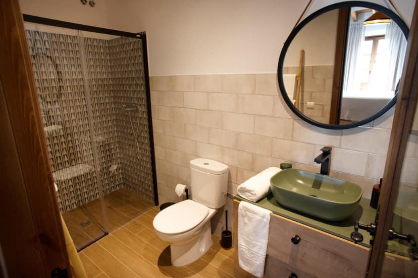 Bathroom in Casa Rural Candelas with wood floor, green vessel sink, and patterned shower.
