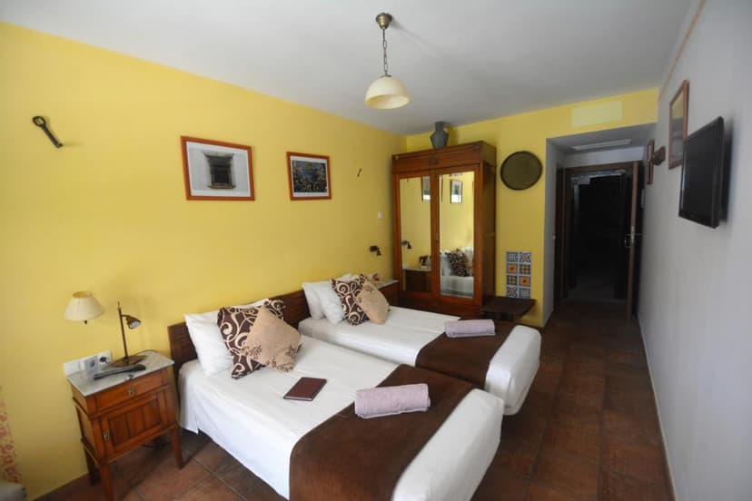 Twin beds with white linens and brown accents in a room with yellow walls at Hotel Posada San Marcos.