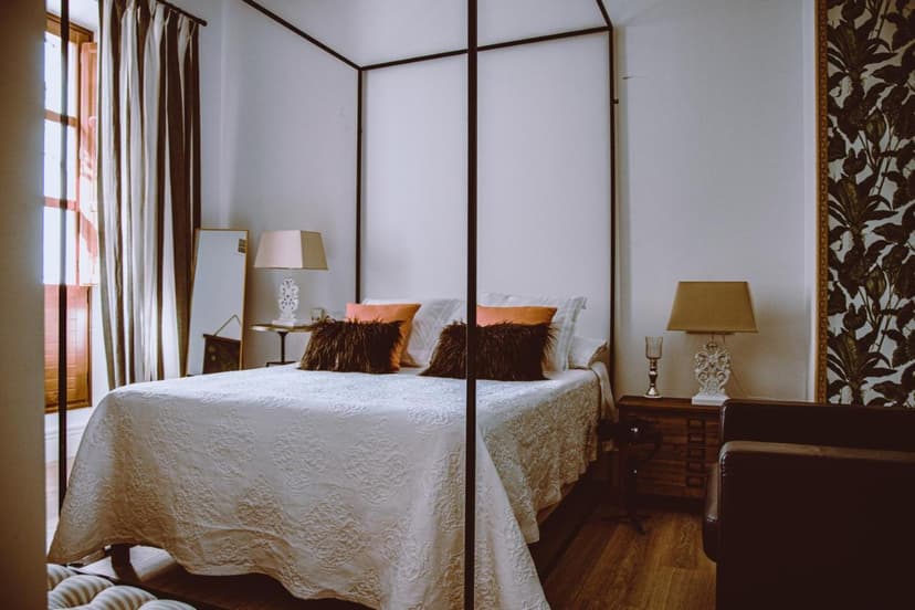 Four-poster bed with white quilt and orange pillows in a room at Hotel Luz Almonaster.