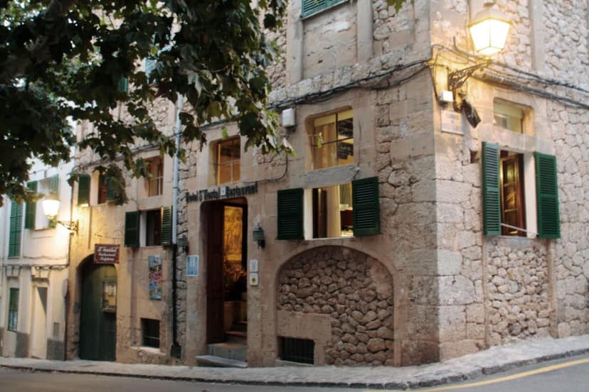 Stone hotel and restaurant entrance in Esporles with green shutters and illuminated street lamp.