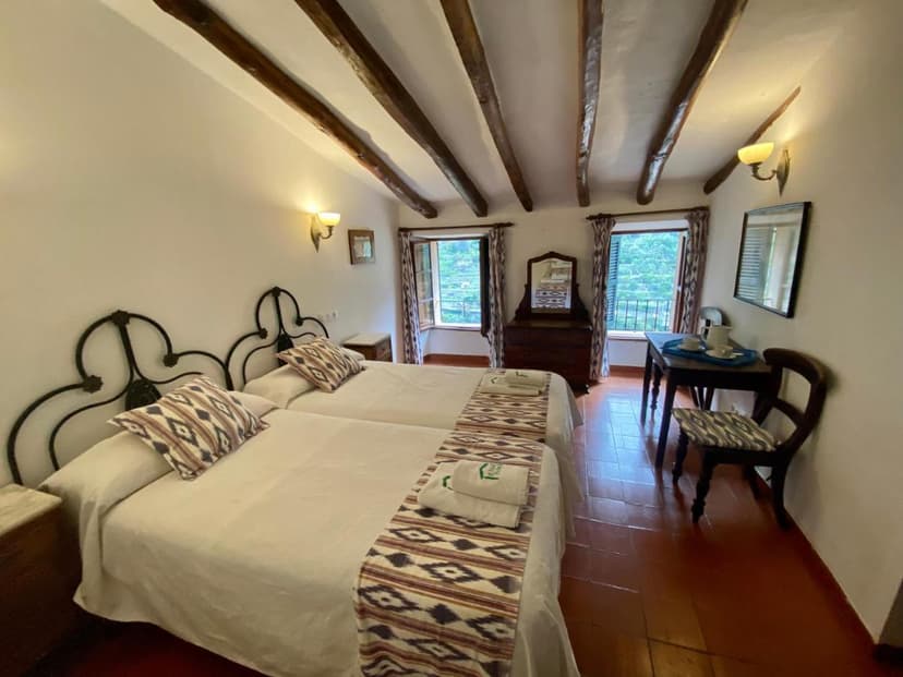 Twin beds in Hostal Villa Verde room with wood beamed ceiling and balcony view