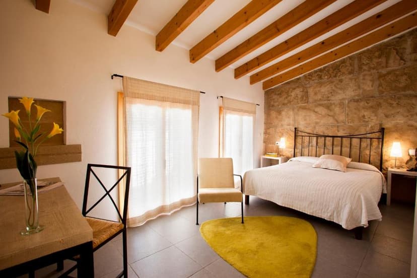 Boutique hotel room with exposed stone wall, wooden beams, and yellow accent rug.