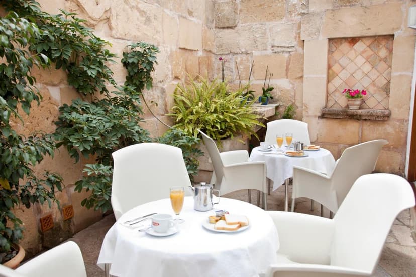 Outdoor breakfast tables with white chairs set against a stone courtyard with lush greenery.