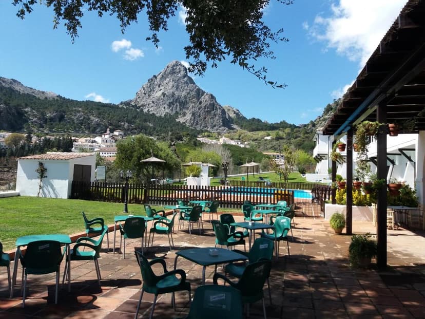 Outdoor patio with green chairs overlooking a mountain village and pool at Villa Turística de Grazalema.