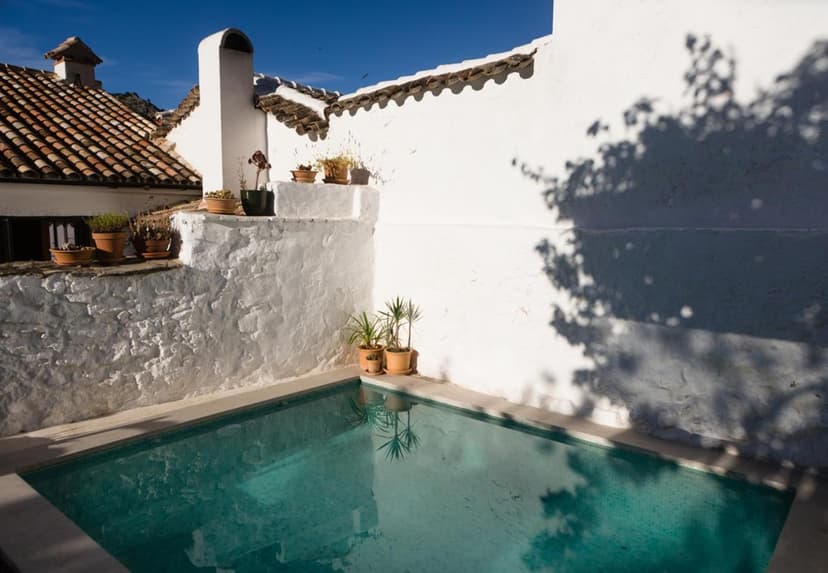 Small turquoise pool surrounded by white stucco walls with potted plants and a tiled roof.