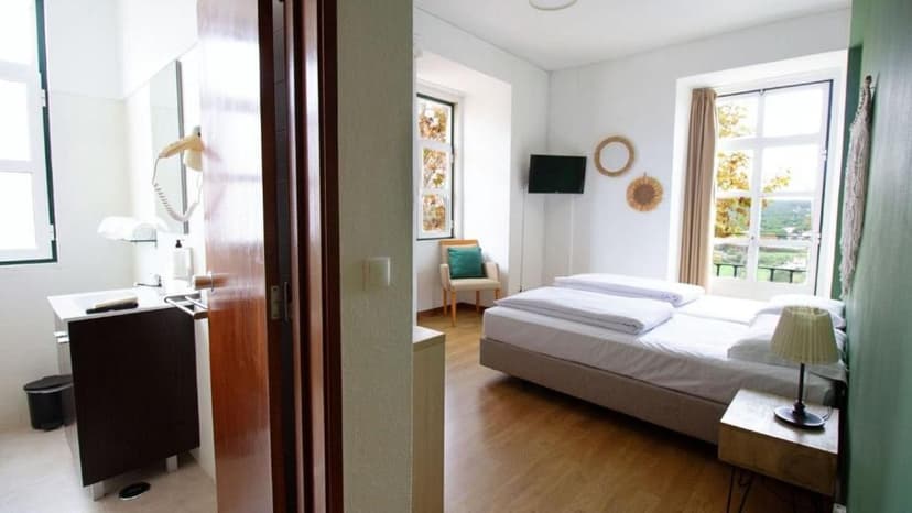 Bright hotel room with twin beds, wood floor, and view of greenery from window.