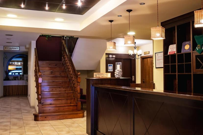Hotel Valle De Izas reception area with dark wood desk, wooden staircase, and wicker pendant lights.