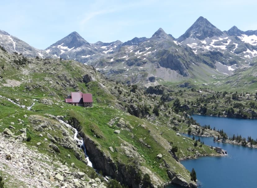 Mountain refuge Refugio de Respomuso near blue alpine lakes with snow-capped peaks.