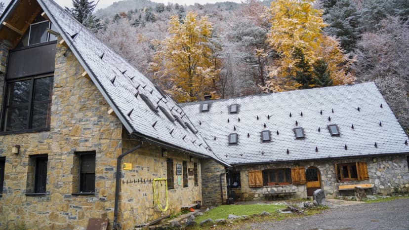Stone refuge building with snow-dusted roof against autumn forest in the mountains