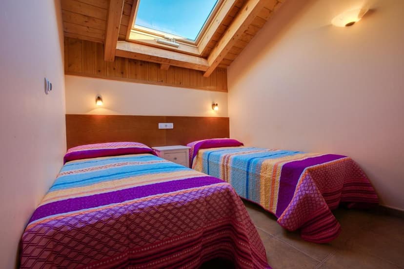 Twin room with colorful striped bedding under a slanted wooden ceiling and skylight.