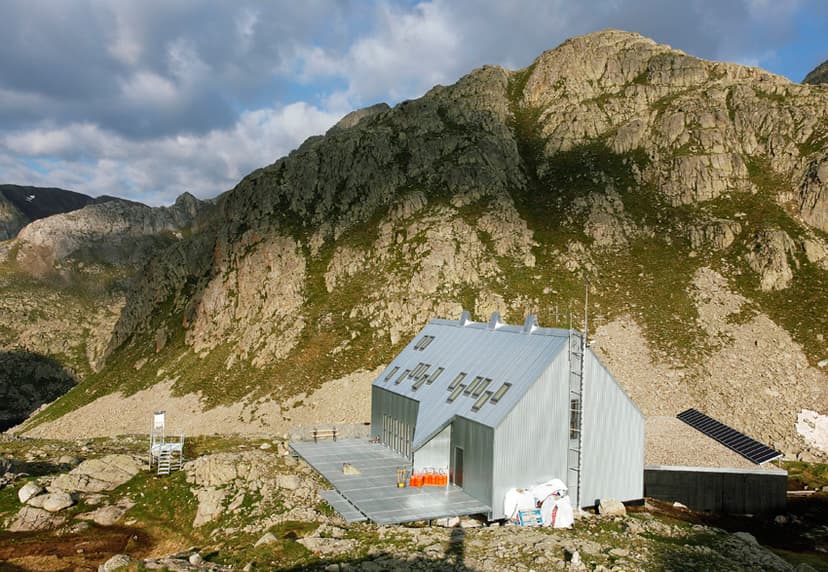 Refuge Cap de Llauset modern mountain hut with metal siding below rocky slopes and cloudy sky.