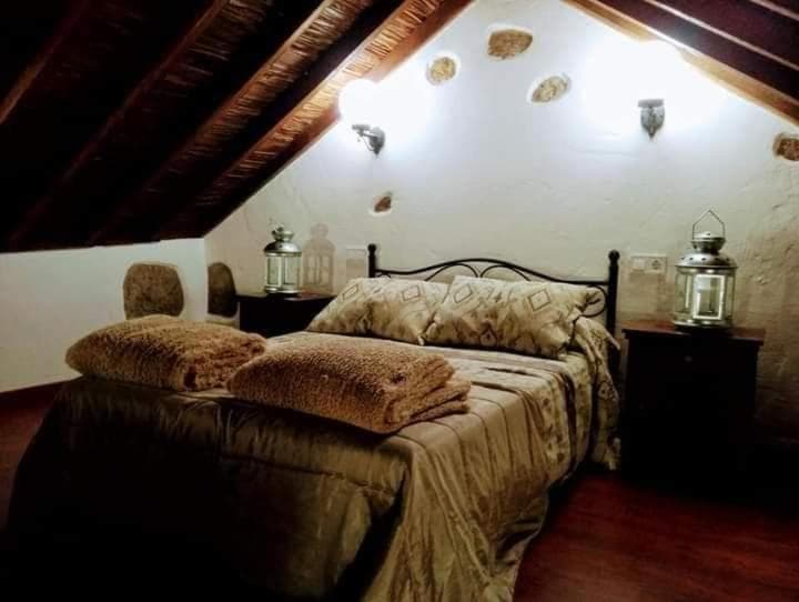 Attic bedroom with dark wood ceiling, white walls, metal bed frame, and rustic lanterns in Santiago de Tunte.