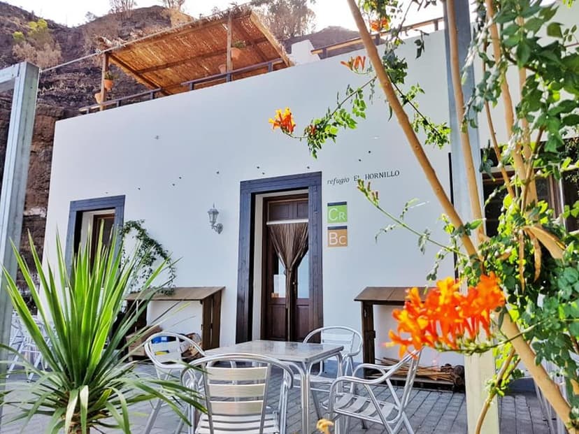 Refugio El Hornillo exterior with patio seating, orange flowers, and steep hillside.