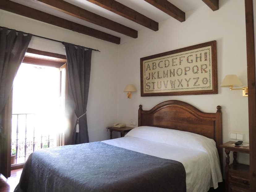 Bedroom with wooden beams, a large alphabet sampler, and a balcony door letting in bright light.