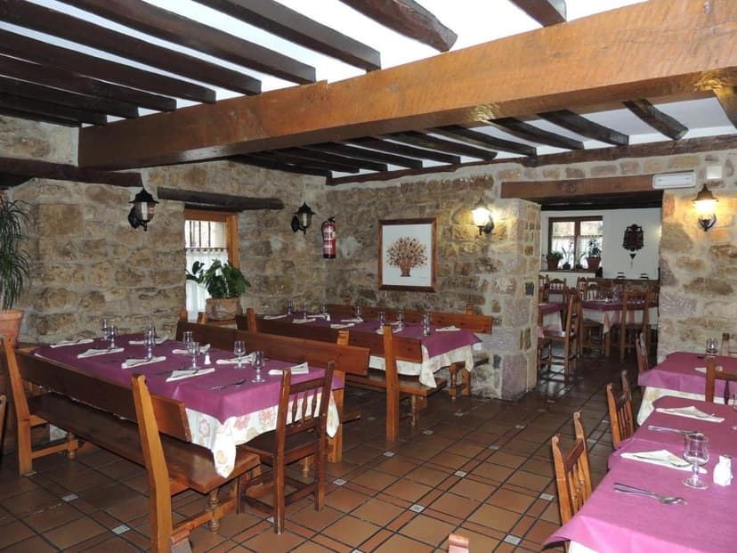 Dining room with stone walls, exposed wooden beams, and set tables with purple tablecloths at Posada Maximo.
