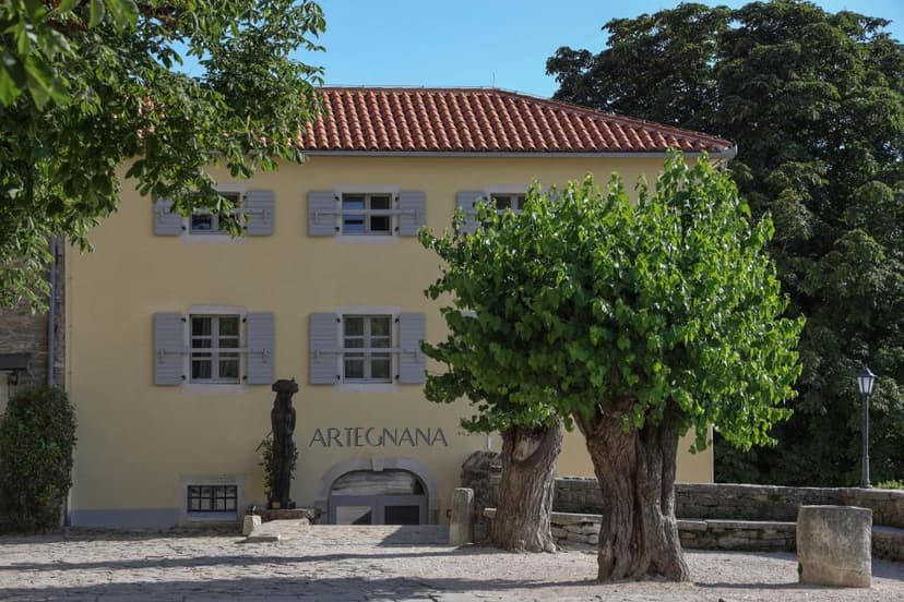 Yellow building with "ARTEGNANA" sign, trees, and cobblestone courtyard