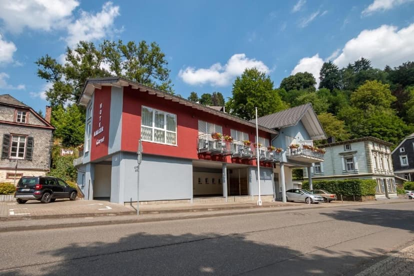Haller Hotel Garni building with red facade, balconies, and parked cars on a sunny day.