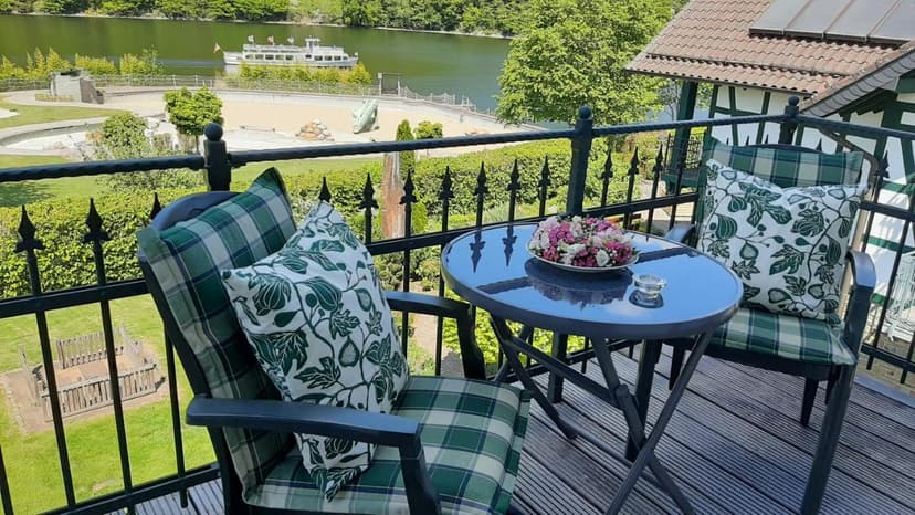 Balcony seating with lake view, boat on water, and green hillside in summer