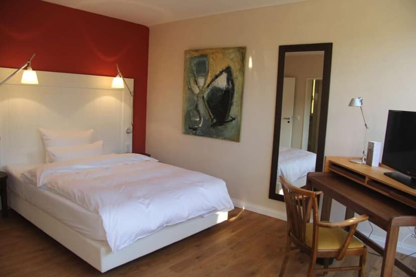 Hotel room with white bedding, wood floor, red accent wall, and mirror reflecting another bed.