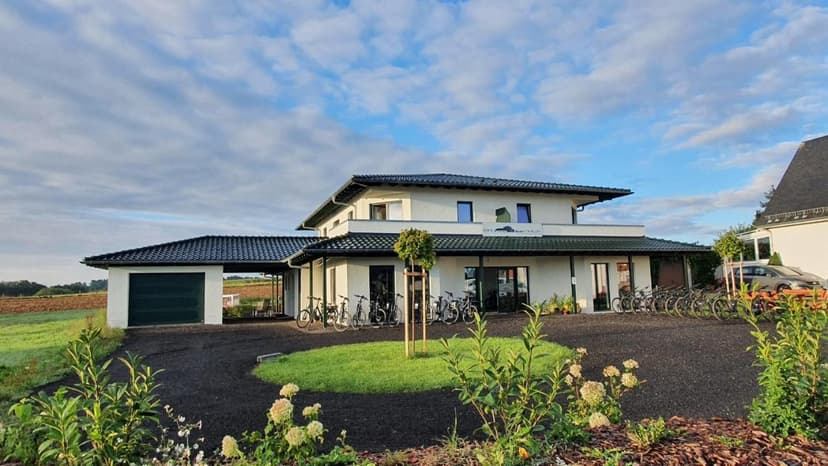 Pension building with many bicycles parked outside, set against fields under a cloudy sky.