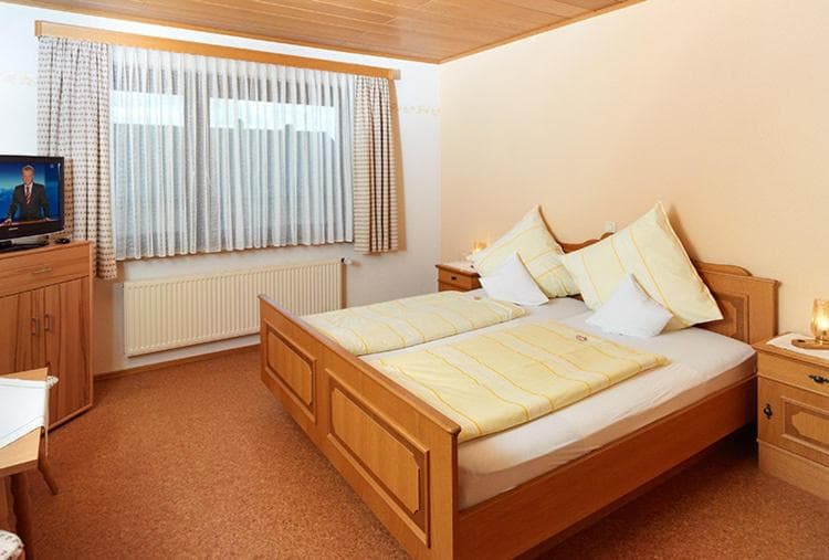 Double bed with yellow bedding in a hotel room with wood furniture and cork flooring.
