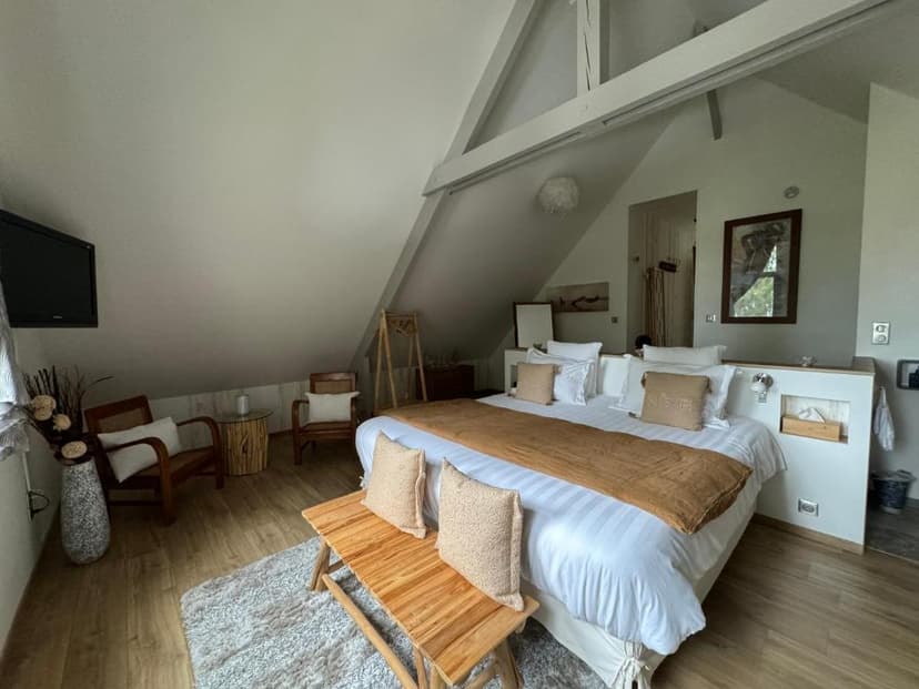 Bedroom under a sloped attic ceiling with a large bed and wooden furniture, near Mont Saint-Michel.