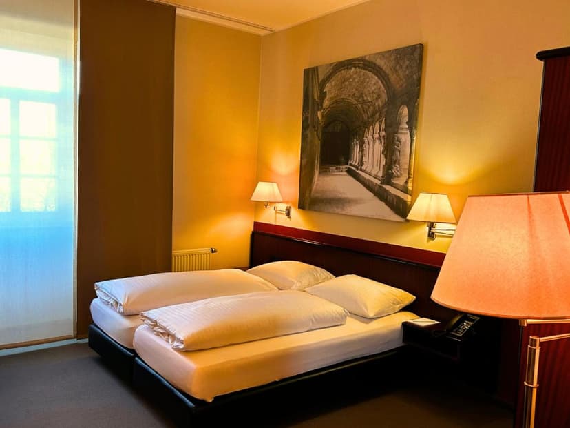 Twin beds in a warmly lit hotel room with artwork of an arched hallway.