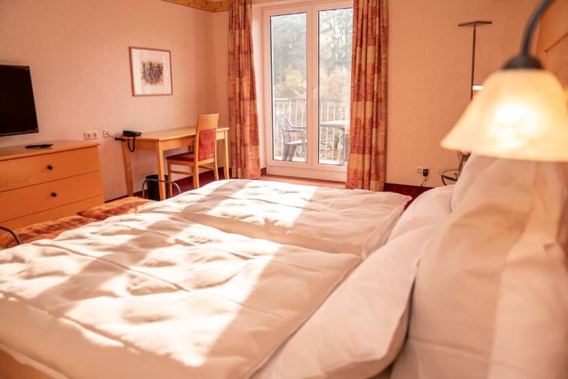 Hotel room with twin beds, wooden furniture, and balcony access through glass doors.