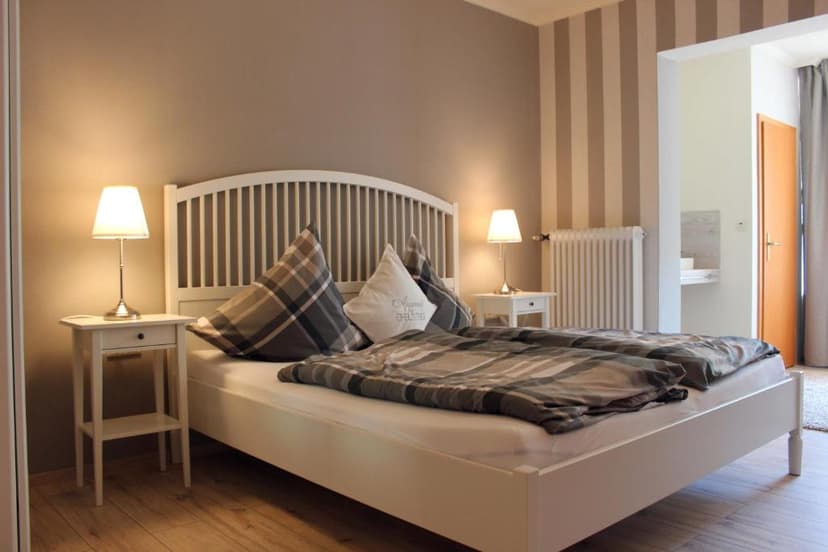Bedroom with white bed, plaid bedding, and illuminated bedside lamps.