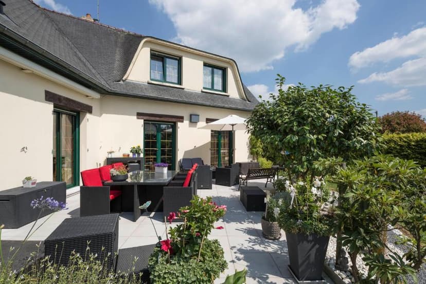 Patio with black wicker dining set and red cushions outside a house with green trim under a blue sky.