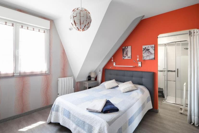 Bedroom in attic space with orange accent wall, white and red wallpaper, and ensuite shower stall.