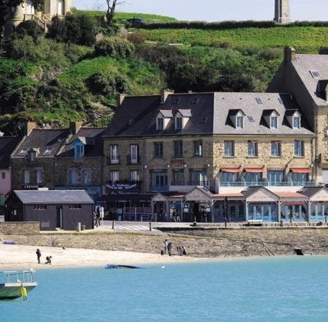 Hotel and stone buildings line the shore above a small beach with people, La Mère Champlain.