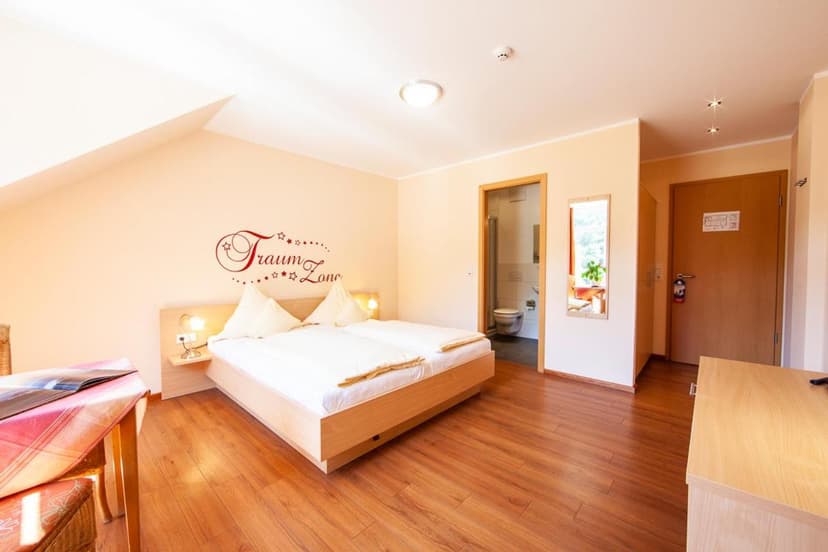 Hotel room with wooden floor, double bed, wall decal, and view into a bathroom.