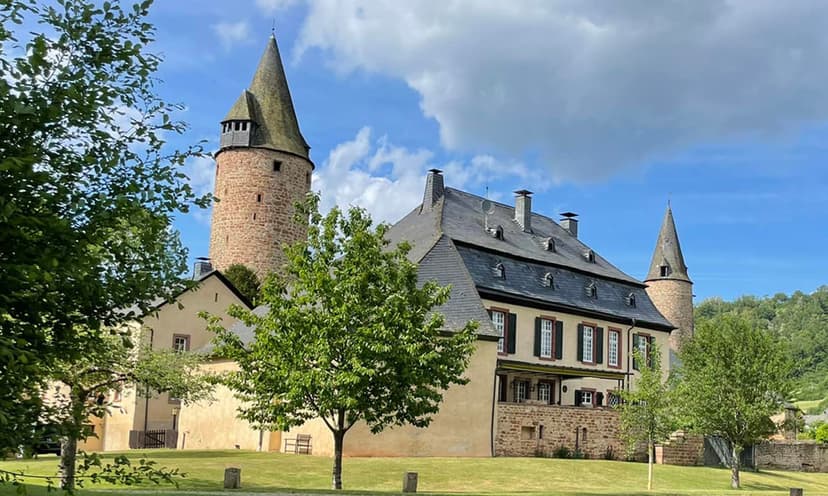 Historic stone castle with conical towers and green lawn under a partly cloudy sky.