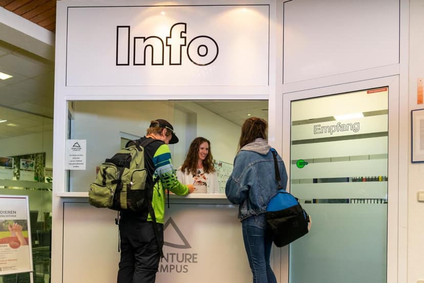Adventure Campus reception desk with staff assisting two guests with backpacks.