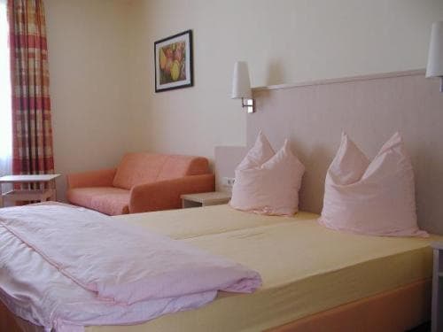 Twin beds with pink linens, orange sofa, and framed art in Gasthof zum Brunnen room.