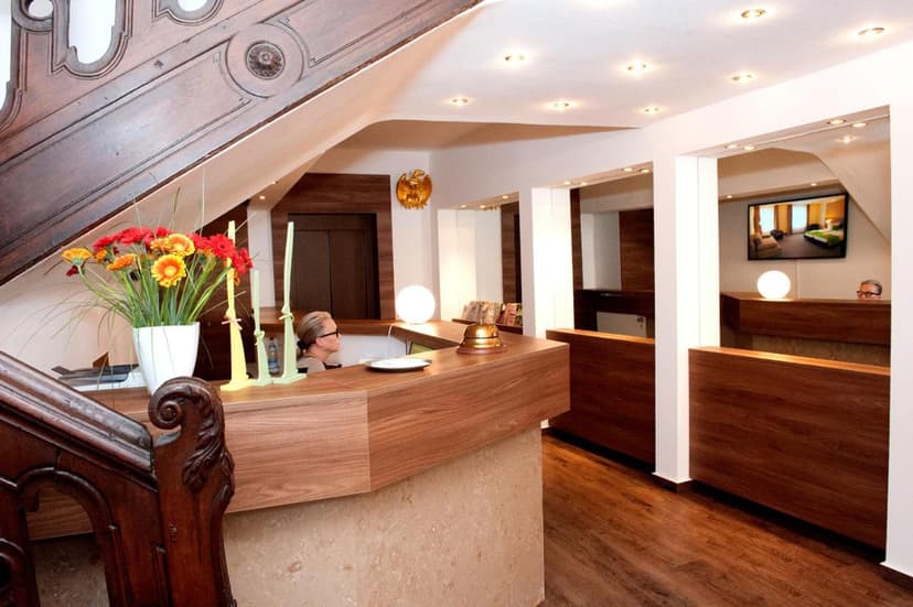Hotel Adler reception area with wooden desk, flowers, and a staff member visible.