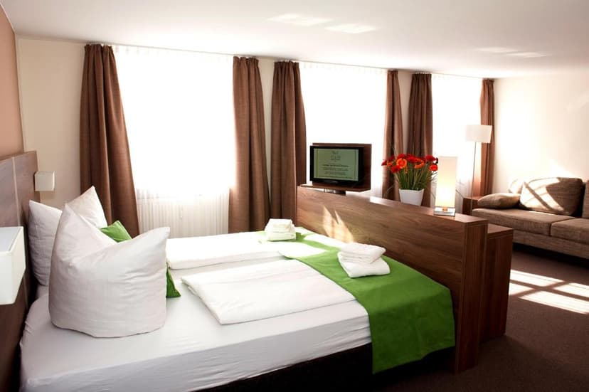 Hotel room with twin beds, white linens, green runner, and a mounted television.