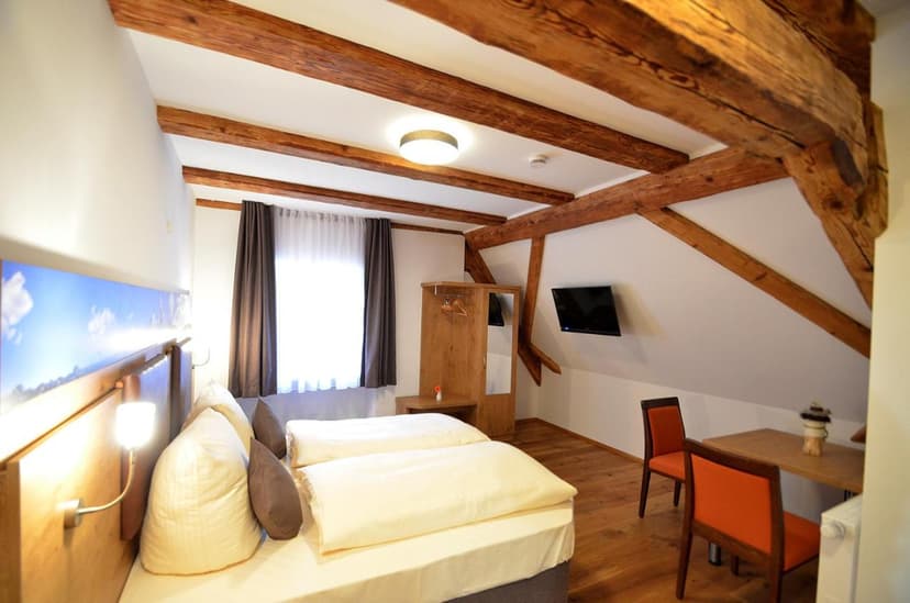 Attic guest room with exposed wooden beams, twin beds, and a small dining area.