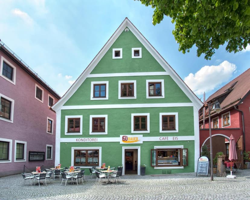 Green Konditorei and Café Eis building with outdoor seating on cobblestone square.