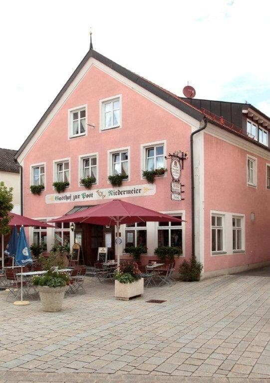 Hotel zur Post Garni, a pink building with outdoor cafe seating on a paved square.