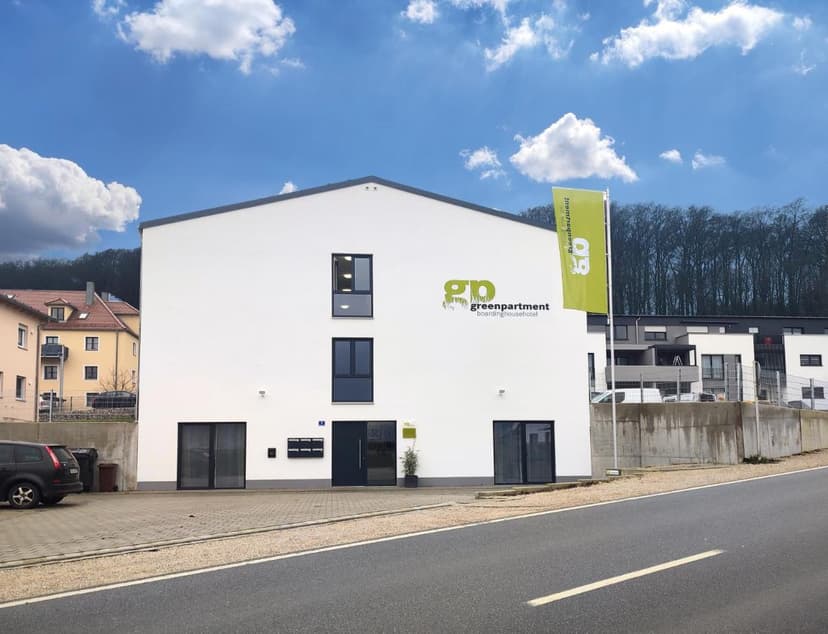 White Greenapartment boarding house exterior with flag, Kelheim, under blue sky.
