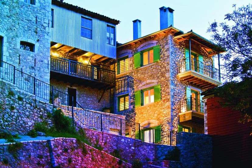 Stone guesthouse with illuminated windows and green shutters, built into a hillside at dusk