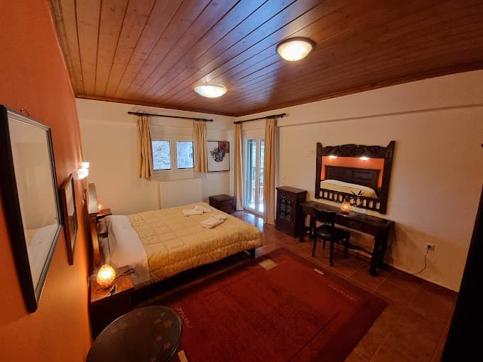 Cozy guest room with wooden ceiling, queen bed, and ornate dark wood vanity near Elati Inn.